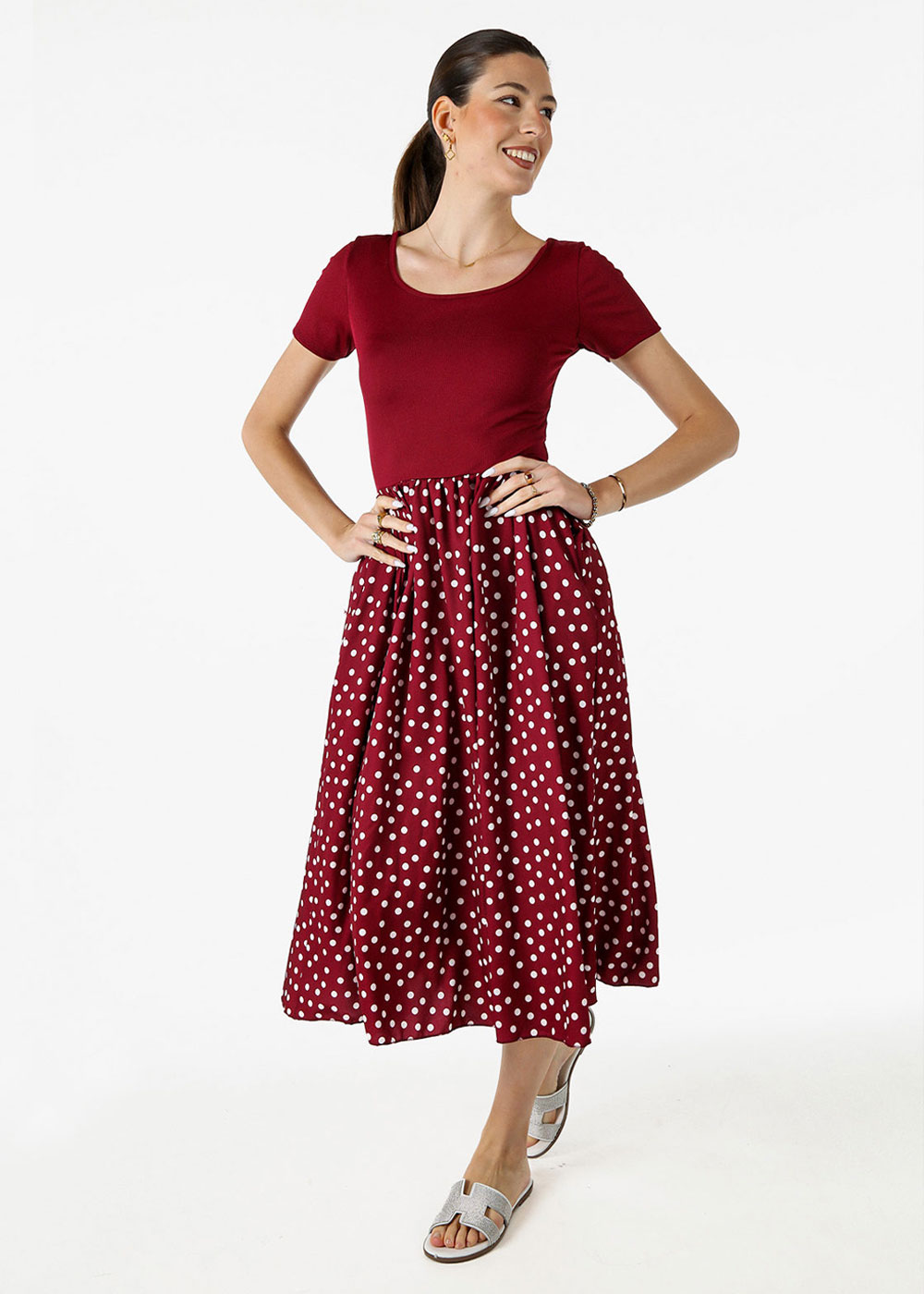Woman in burgundy short-sleeve top and burgundy white polka-dot midi skirt, smiling with hands on hips and sandals