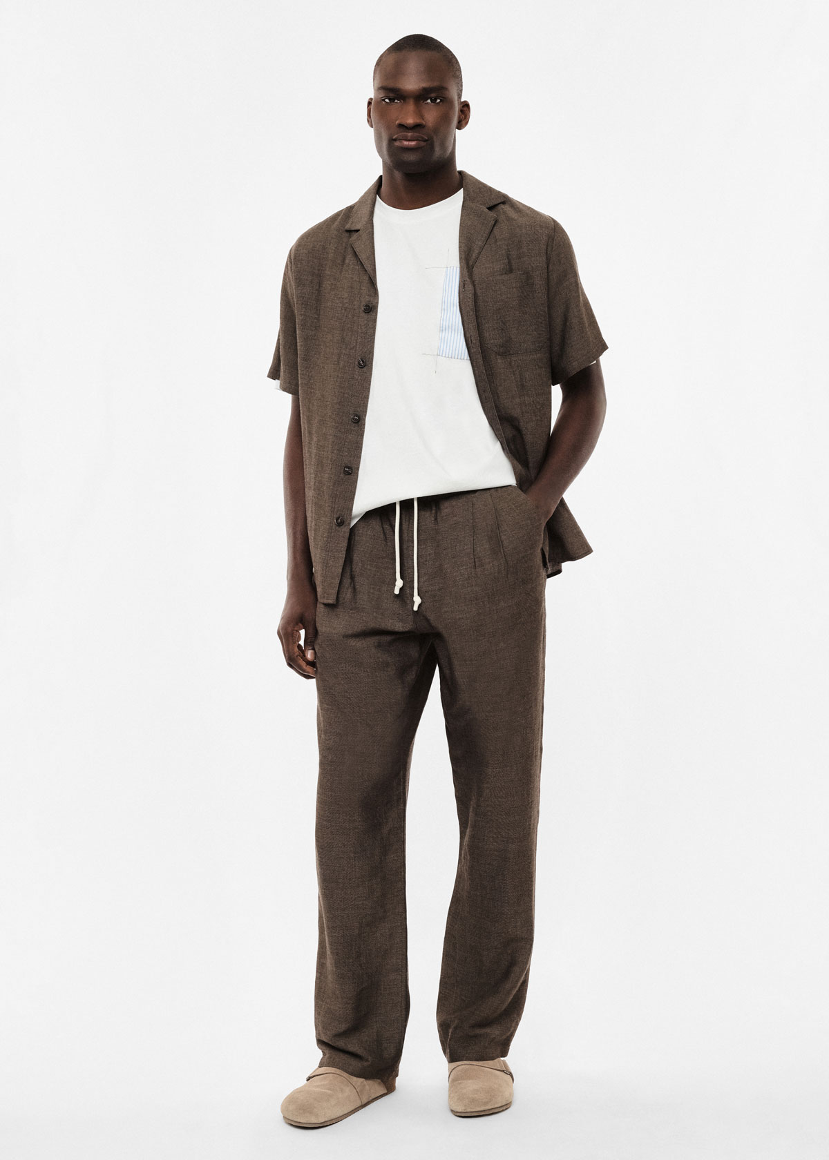 Tall man wearing brown linen short-sleeve shirt and matching drawstring trousers, white T-shirt with pocket and beige slippers