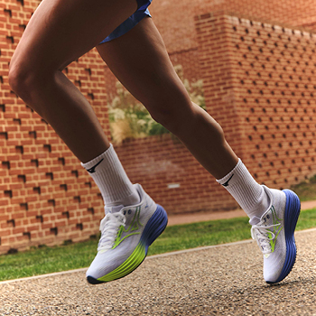 Close-up of runner's legs in white trainers with blue-green soles mid-stride on a paved path beside a brick wall