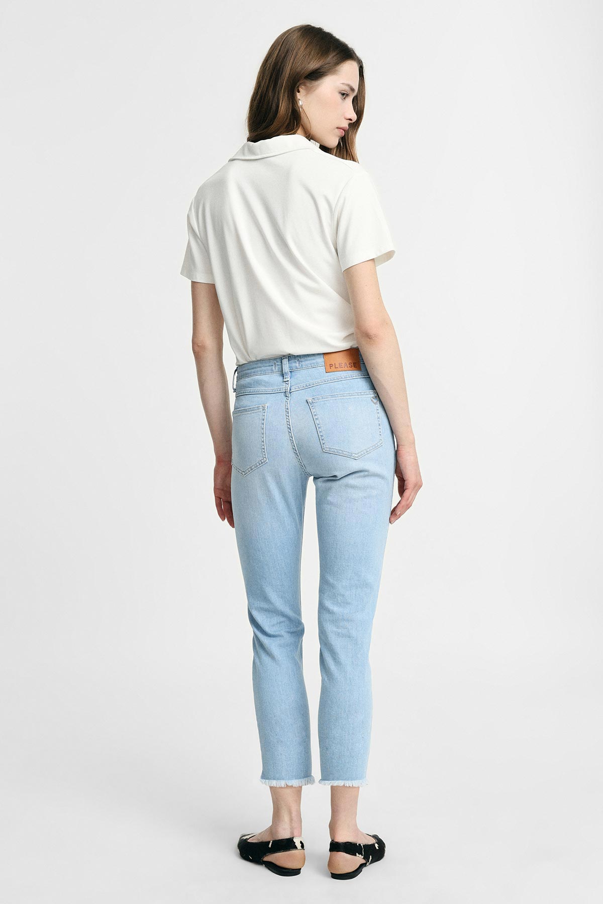 Woman viewed from back wearing a white short-sleeve top and light-wash cropped jeans with frayed hems and black sandals