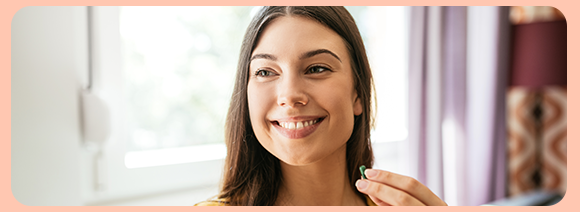 “Donna sorridente mentre tiene una capsula vicino al viso, in un ambiente luminoso.” “Donna sorridente mentre tiene una capsula vicino al viso, in un ambiente luminoso.”