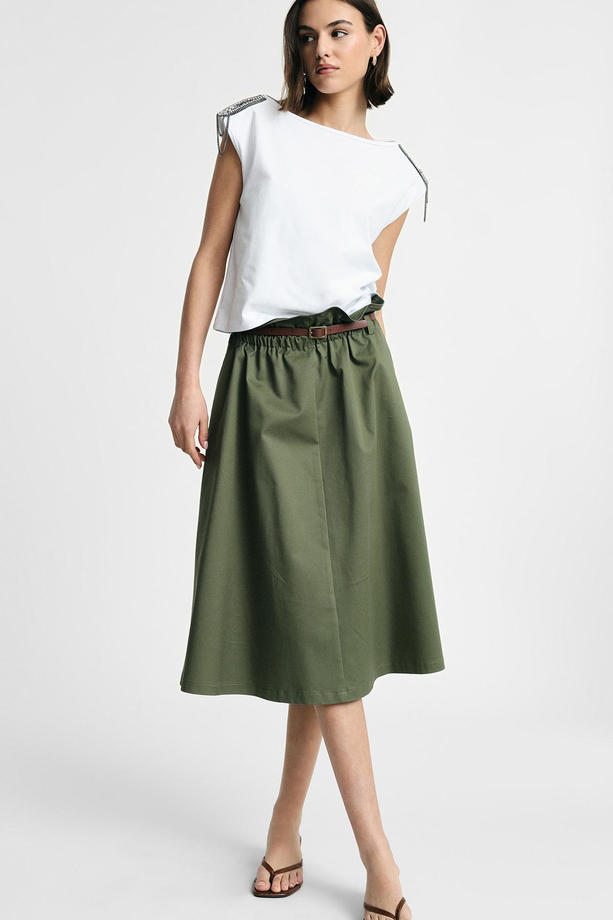 Woman modelling white sleeveless top with embellished shoulders and olive green A-line midi skirt with brown belt, standing