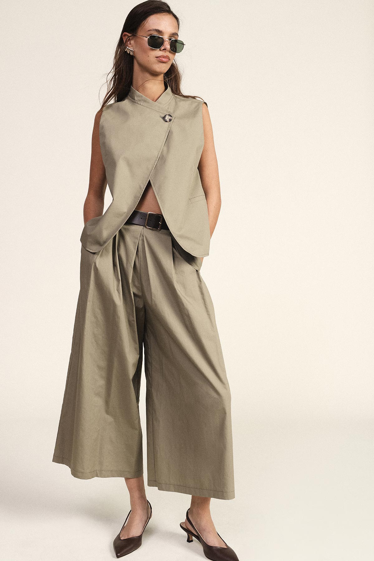 Woman modelling khaki sleeveless wrap top and wide-leg culotte trousers with belt, sunglasses and low-heeled slingback shoes
