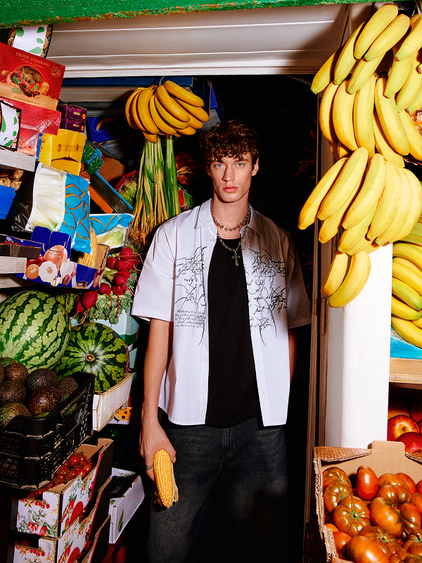 Modello con camicia a maniche corte e T-shirt nera in un negozio di frutta.