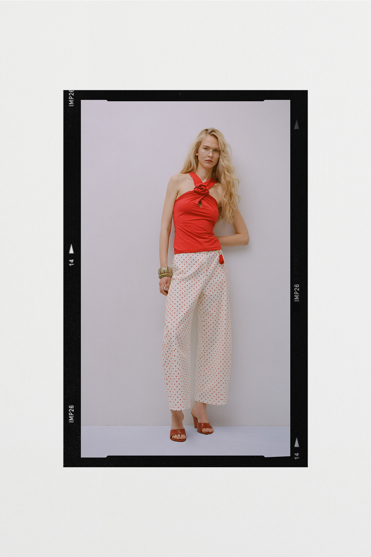 Young woman modelling a red halter-neck top and white polka-dot wide-leg trousers, standing against a pale studio background