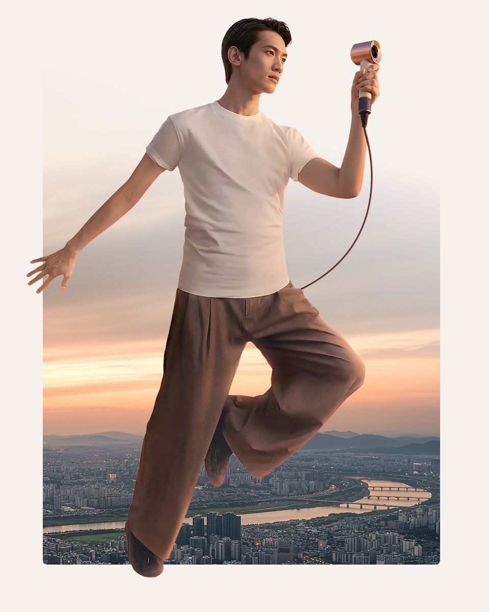 Una modella salta a mezz’aria con in mano l’asciugacapelli Dyson Supersonic Travel.