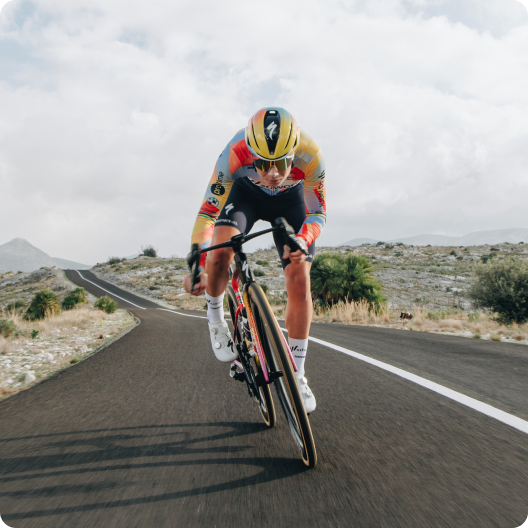 Cyclist in yellow helmet and colourful skinsuit descending on an aerodynamic road bike along winding mountain road under cloudy sky