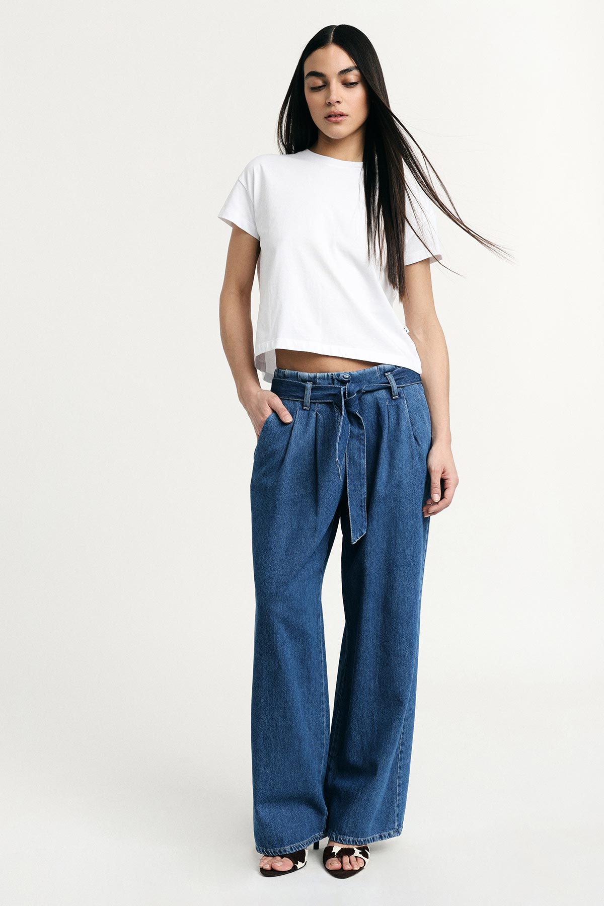 Young woman modelling white cropped T-shirt and high-waist wide-leg denim jeans with tie belt and sandals