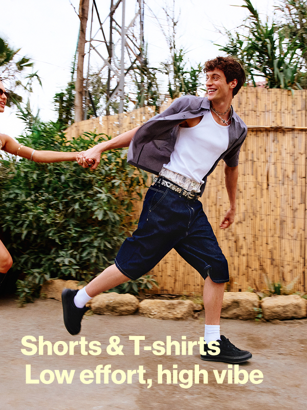 Modello con canotta bianca, camicia a maniche corte e shorts lunghi; scritta Shorts & T-shirts Low effort, high vibe.