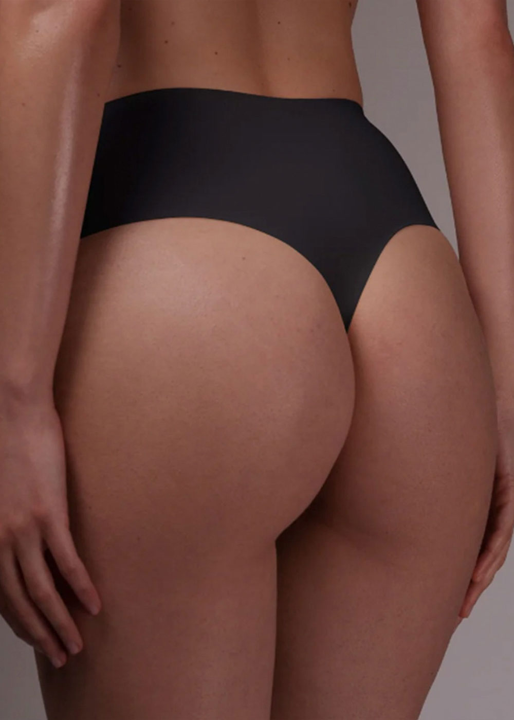 Rear view of model wearing black seamless high-waist thong underwear, showing smooth fit on hips and buttocks