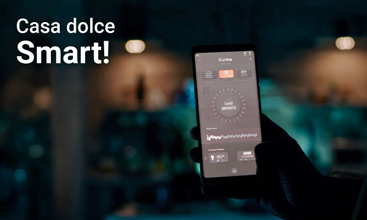 Hand holding smartphone showing smart-home app controls for kitchen lights in a dim modern kitchen, with 'Casa dolce Smart!' text visible