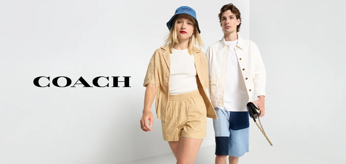 Due modelle camminano su una superficie bianca. Una indossa un completo beige con pantaloni corti e una maglietta abbinata, l'altra una maglietta bianca e pantaloni corti di jeans.