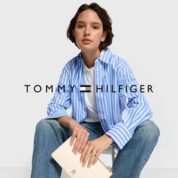Camicia a maniche lunghe a righe blu e bianche, t-shirt bianca, jeans azzurri chiari e sneakers bianche. Tieni in mano una pochette color crema con un logo.