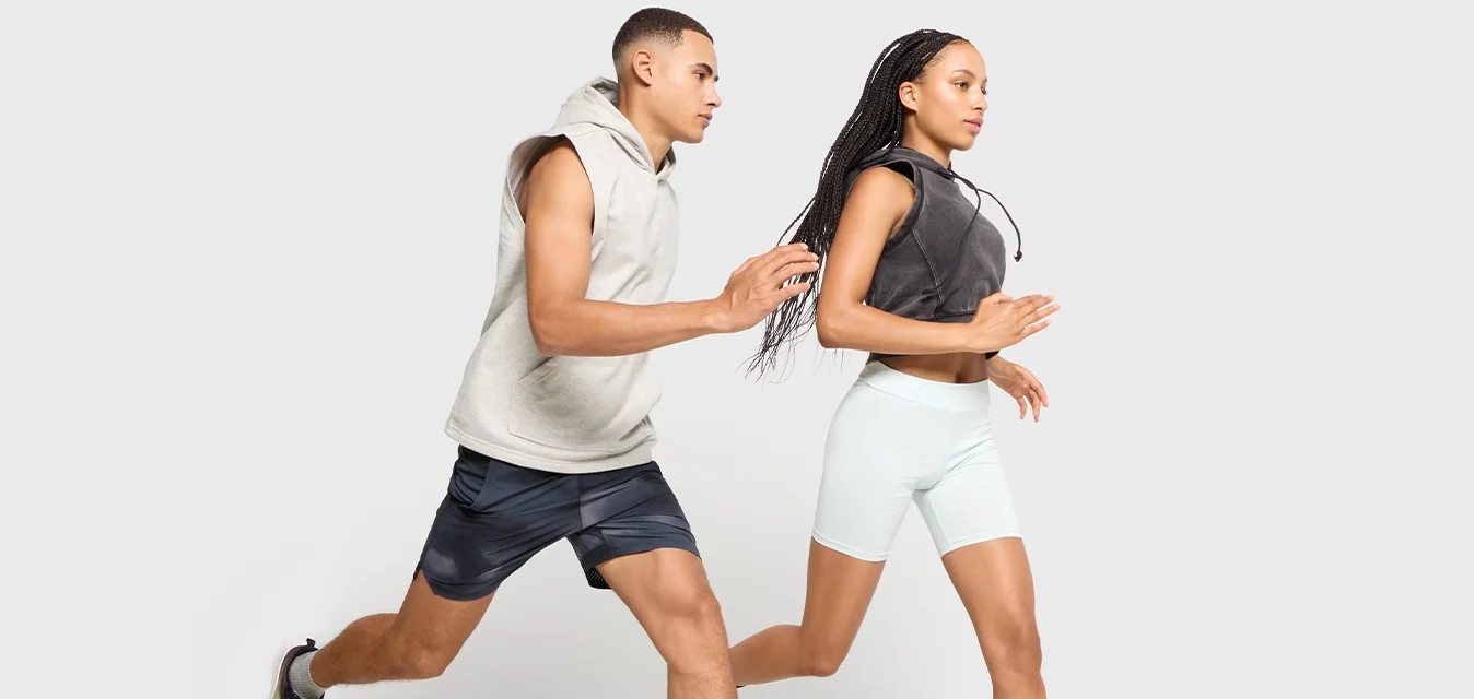 Uomo e donna che corrono fianco a fianco, indossando abbigliamento sportivo, su uno sfondo grigio chiaro.