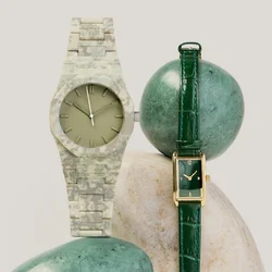 Due orologi da polso, uno con cinturino in pelle verde e quadrante rettangolare, l'altro con cinturino mimetico e quadrante rotondo, esposti su delle pietre.