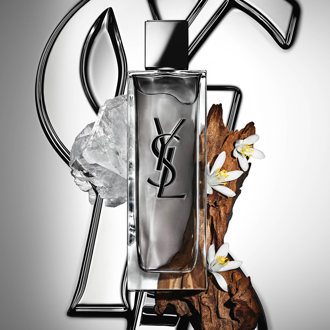 Flacone di profumo YSL MYSLF circondato da roccia minerale, legno e fiori bianchi.