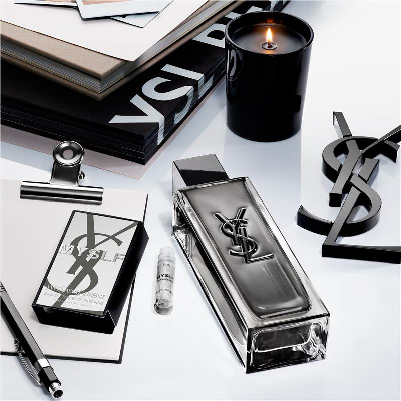 Flacone di profumo, candela e accessori YSL MYSLF su una superficie bianca.