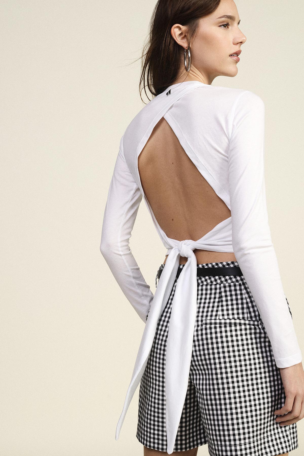 Woman modelling white long-sleeve open-back tie top with bow and black-and-white gingham shorts