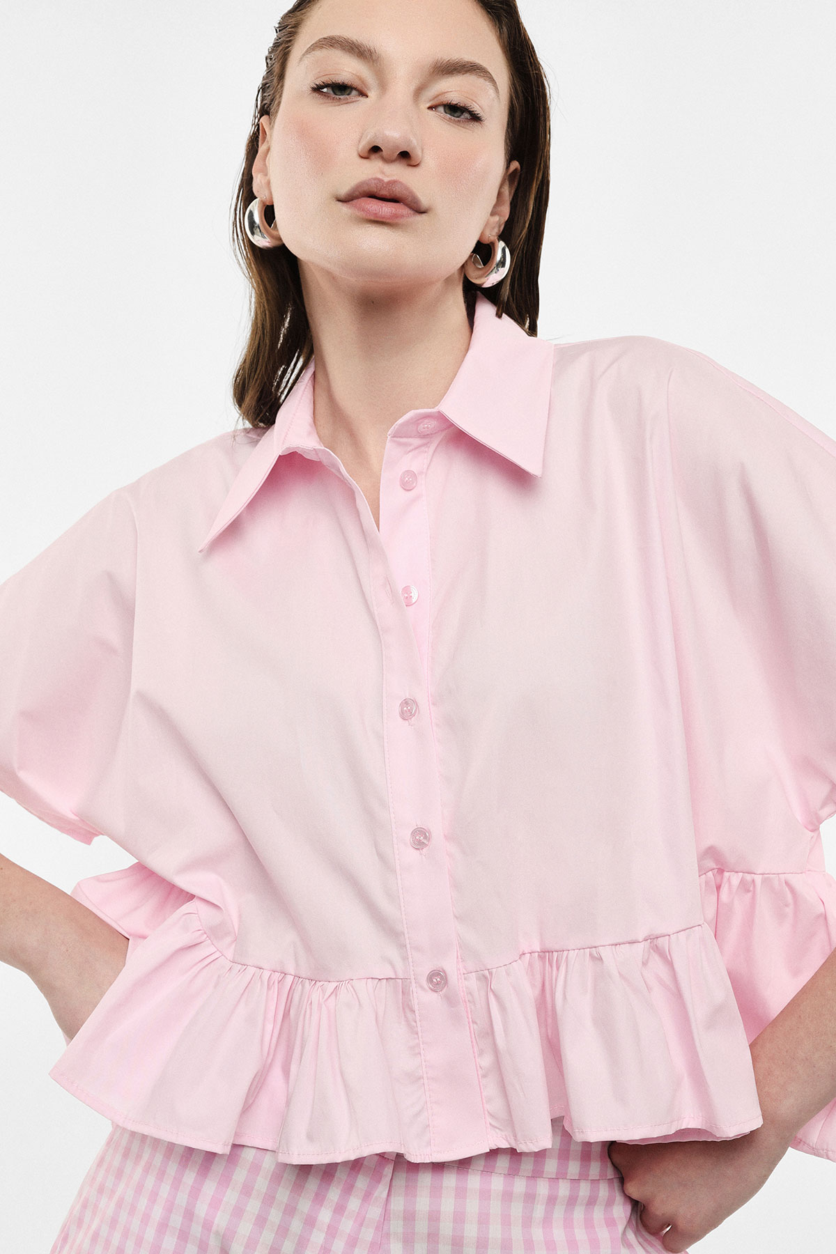 Close-up fashion portrait of a woman wearing a pink ruffled button-up blouse, gingham skirt and silver hoop earrings