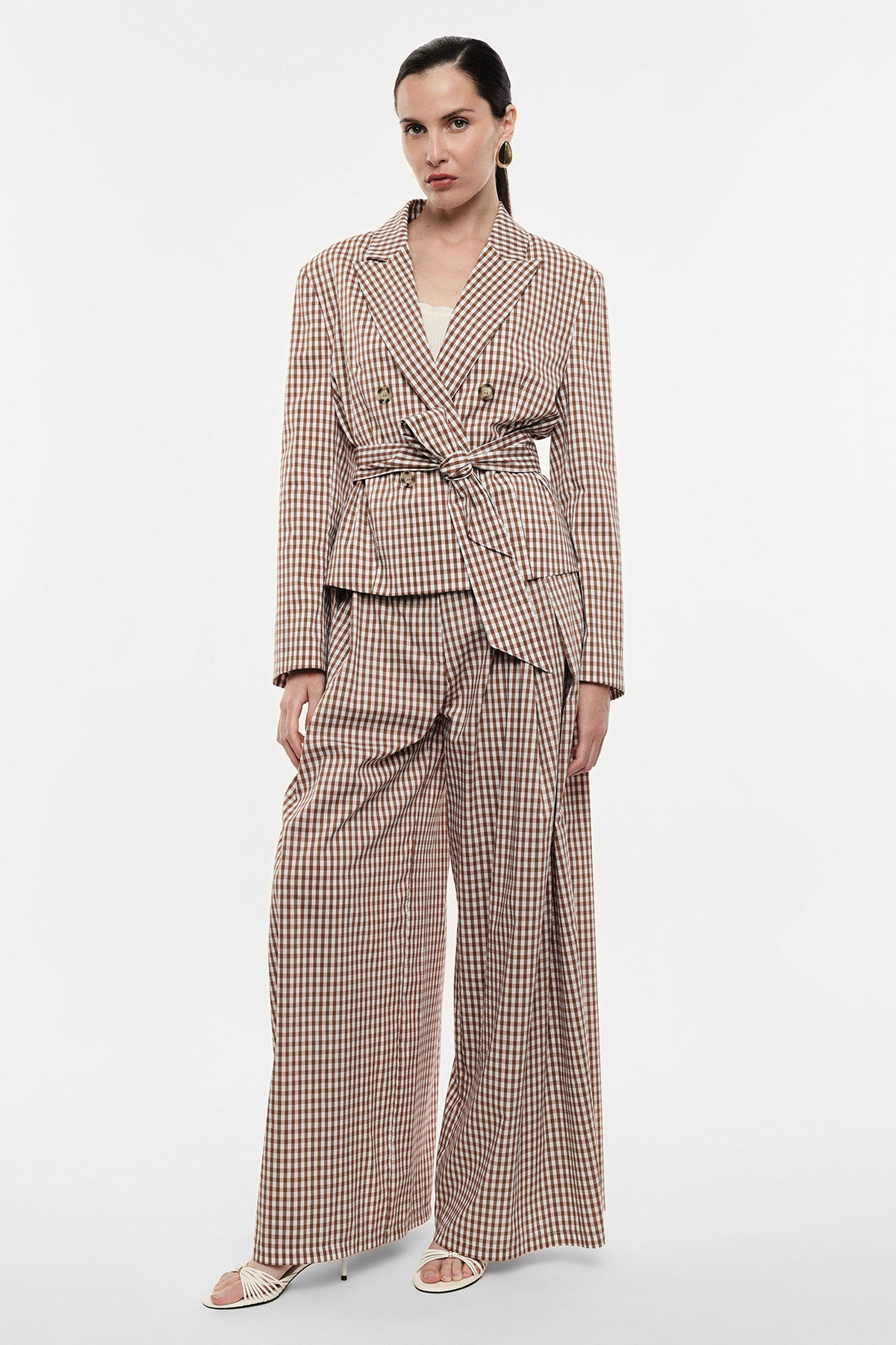 Model wearing brown gingham belted double-breasted blazer and wide-leg trousers with white camisole, gold hoop earrings and sandals