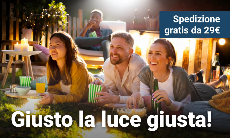 Three friends lying on grass at an evening outdoor movie night, smiling with popcorn, drinks and warm string lights