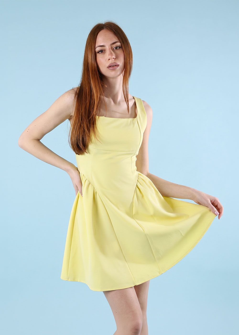 Young woman model in a sleeveless yellow dress posing against a pale blue studio background