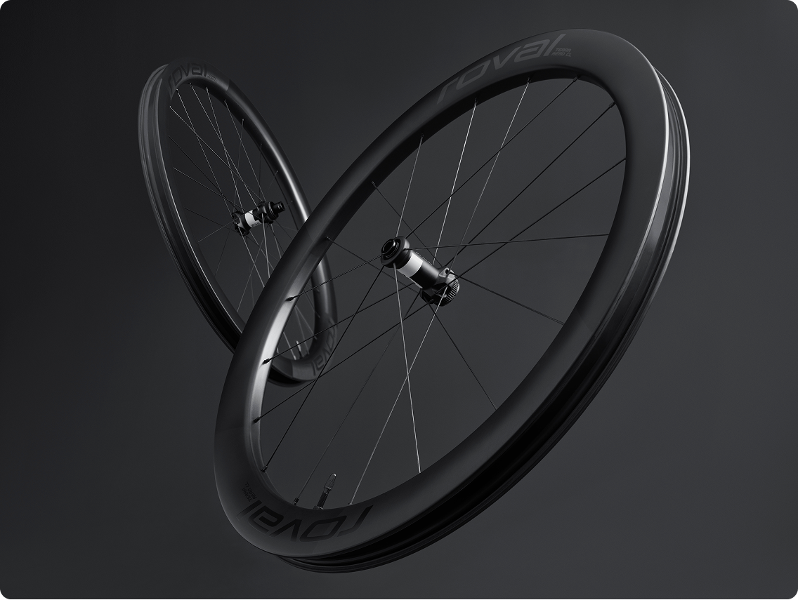 Pair of matte black carbon road bike wheels with deep-section rims and spokes, Roval logo, isolated on dark background