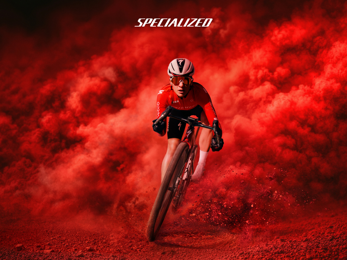 Cyclist in red Specialized kit racing a gravel bike through swirling red dust with the 'Specialized' logo above