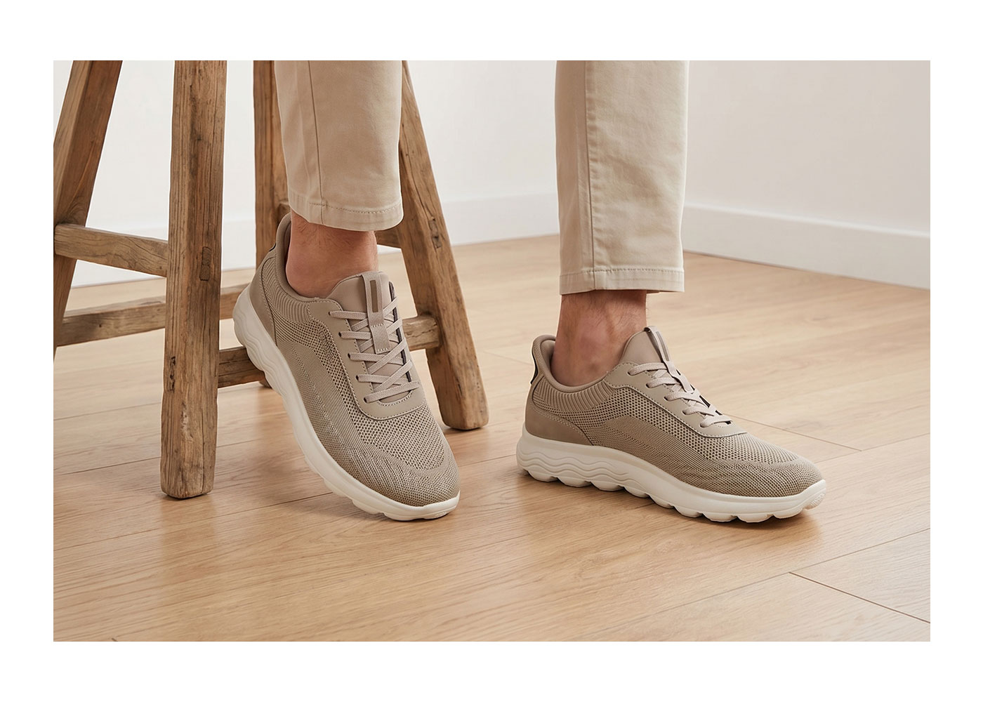 Beige knitted casual trainers with white chunky sole worn with beige chinos on a wooden floor beside a rustic wooden stool