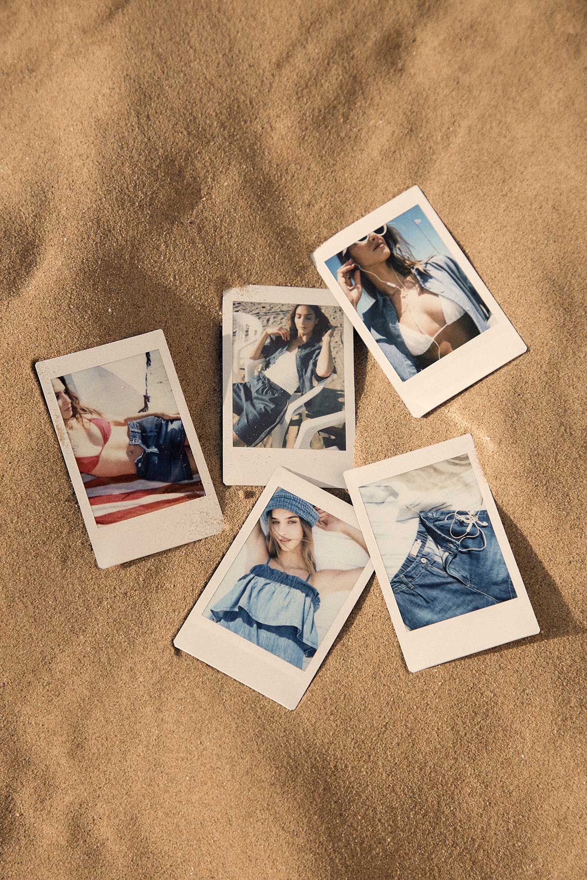 Polaroid photos scattered on sand showing summer fashion: swimsuits, denim jeans and light blue tops on a beach setting