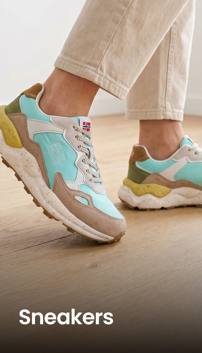 Pair of turquoise and beige chunky sneakers with speckled sole on light wood floor, model wearing cropped cream trousers