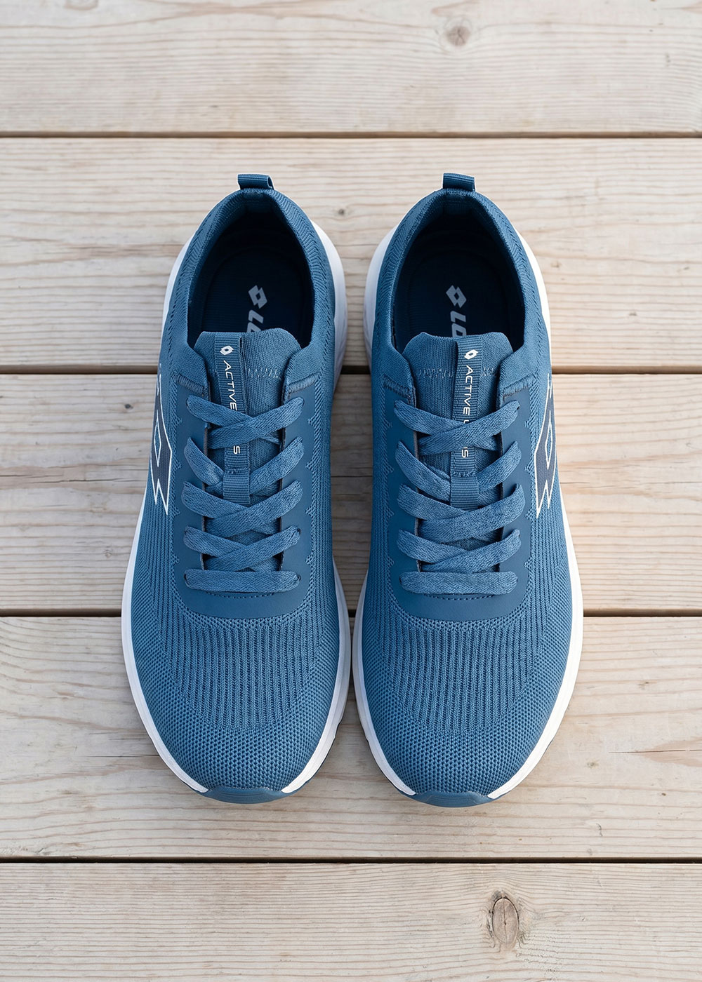 Top-down view of a pair of blue knit running trainers with white soles on a light wooden board floor