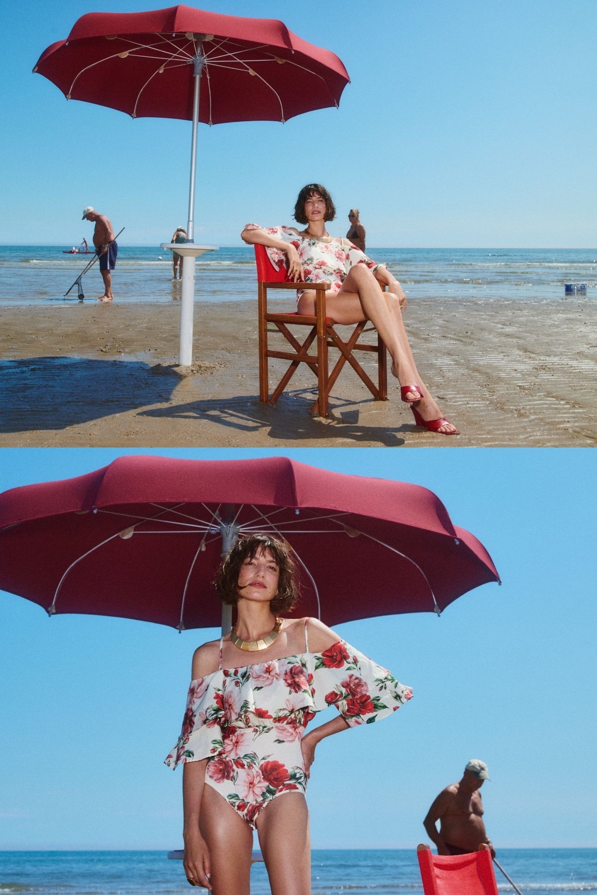 Woman in floral off-shoulder swimsuit under a red beach umbrella on a sandy shore, sea and sunbathers in background