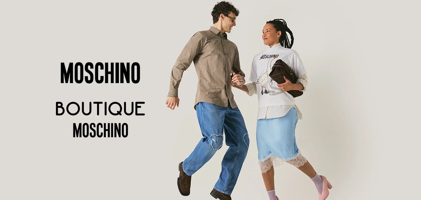 Uomo e donna che si tengono per mano e sorridono, a metà salto su uno sfondo chiaro e semplice; la donna tiene una pochette marrone.