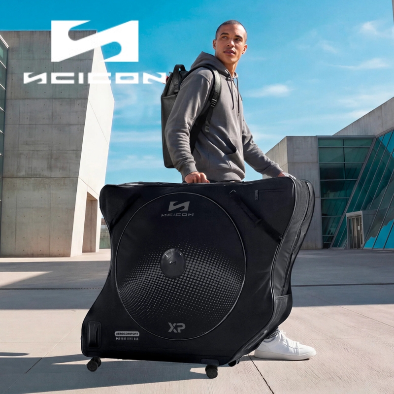 Man pulling large black wheeled bicycle travel bag with backpack in modern urban plaza, brand logo visible