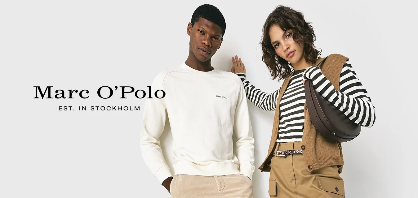 Due adulti appoggiati a un muro bianco, uomo in felpa e pantaloni color crema, donna in top a strisce, gonne beige, gilet, stivali neri, che porta una borsa.
