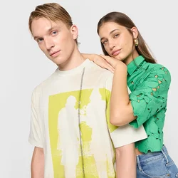 T-shirt grafica color crema con stampa gialla; top verde a maniche corte con intagli floreali. Entrambi abbinati a jeans blu.