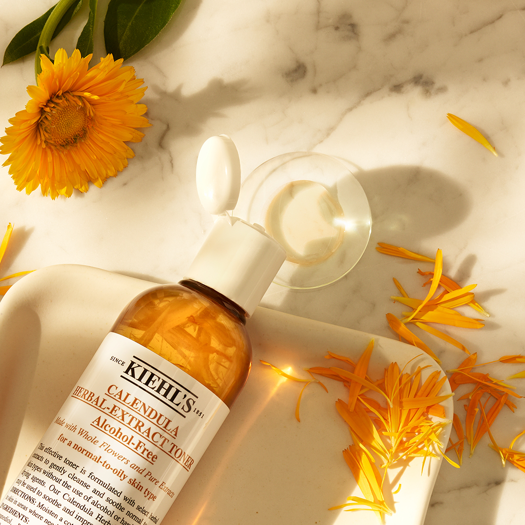 Flacone di Kiehl&rsquo;s Calendula Herbal-Extract Toner Alcohol-Free con petali di calendula su superficie marmorea chiara.
