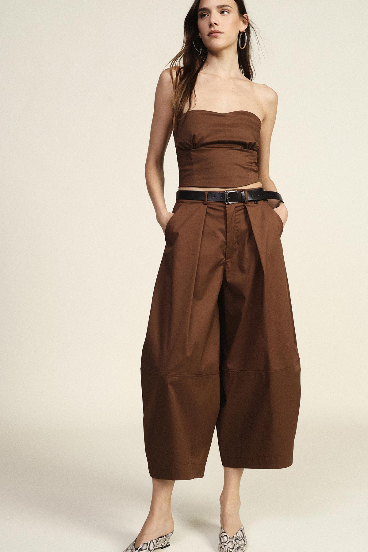 Tall woman modelling a brown strapless top and high-waisted wide-leg culotte trousers with a black belt and snake-print flats, hands in pockets