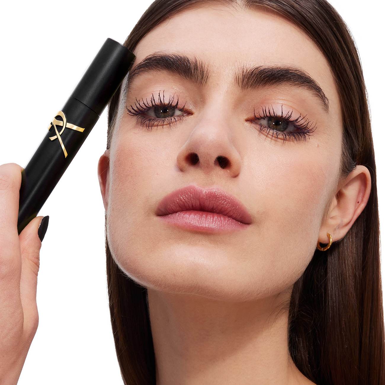 Primo piano di una modella con un incarnato IMPECCABILE, che tiene un mascara YSL LASH CLASH sulla fronte. Sopracciglia audaci e labbra rosa tenue.