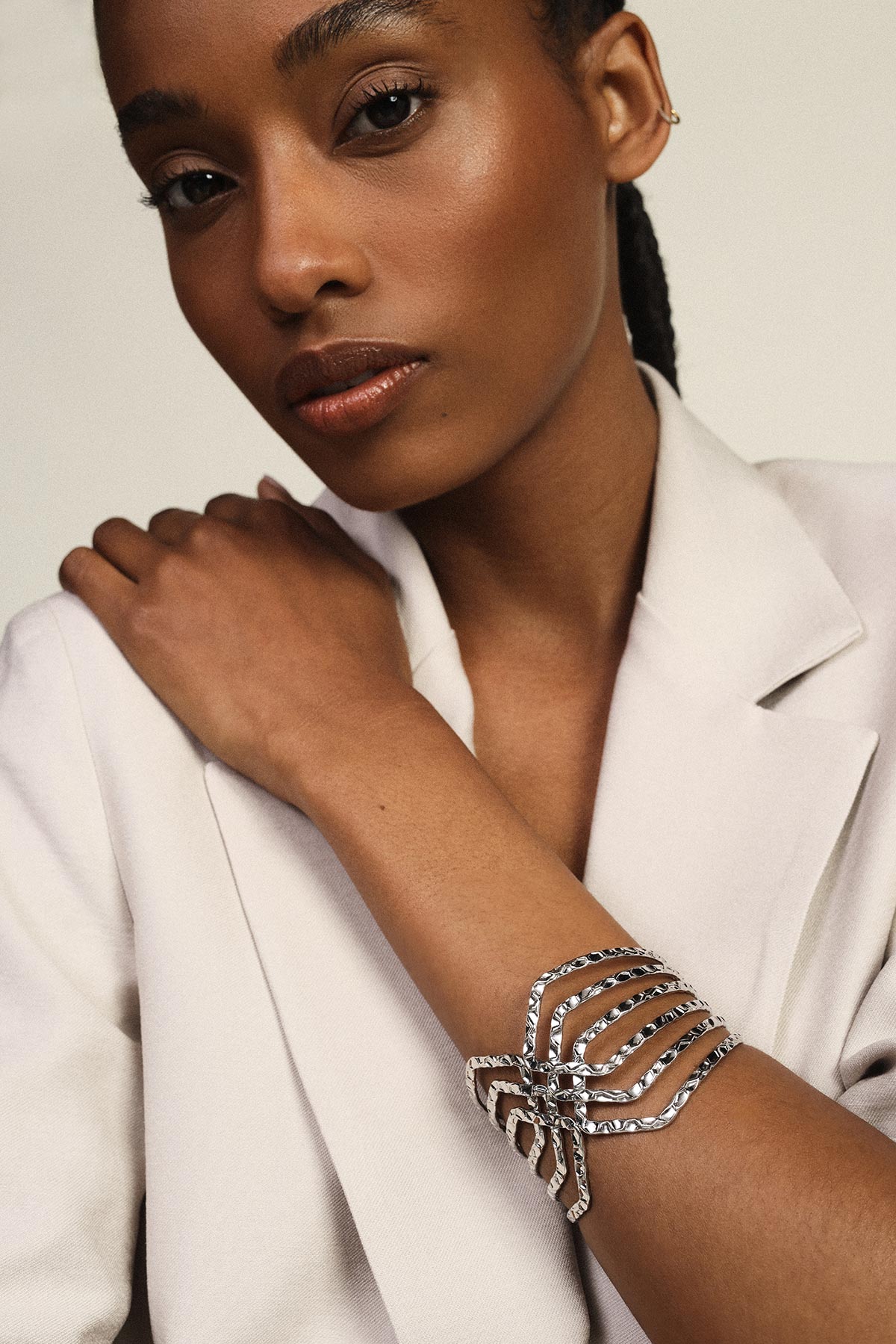 Close-up of woman in cream blazer wearing ornate silver cuff bracelet on her forearm, elegant fashion portrait