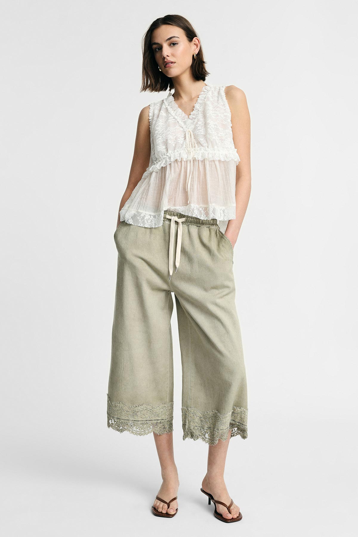 Woman modelling sleeveless white lace peplum top with drawstring wide-leg cropped khaki trousers with lace hem and sandals