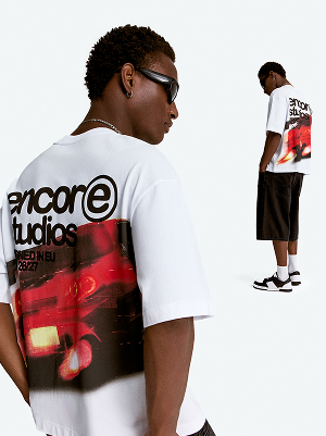 Modello con T-shirt bianca stampata e shorts lunghi neri.