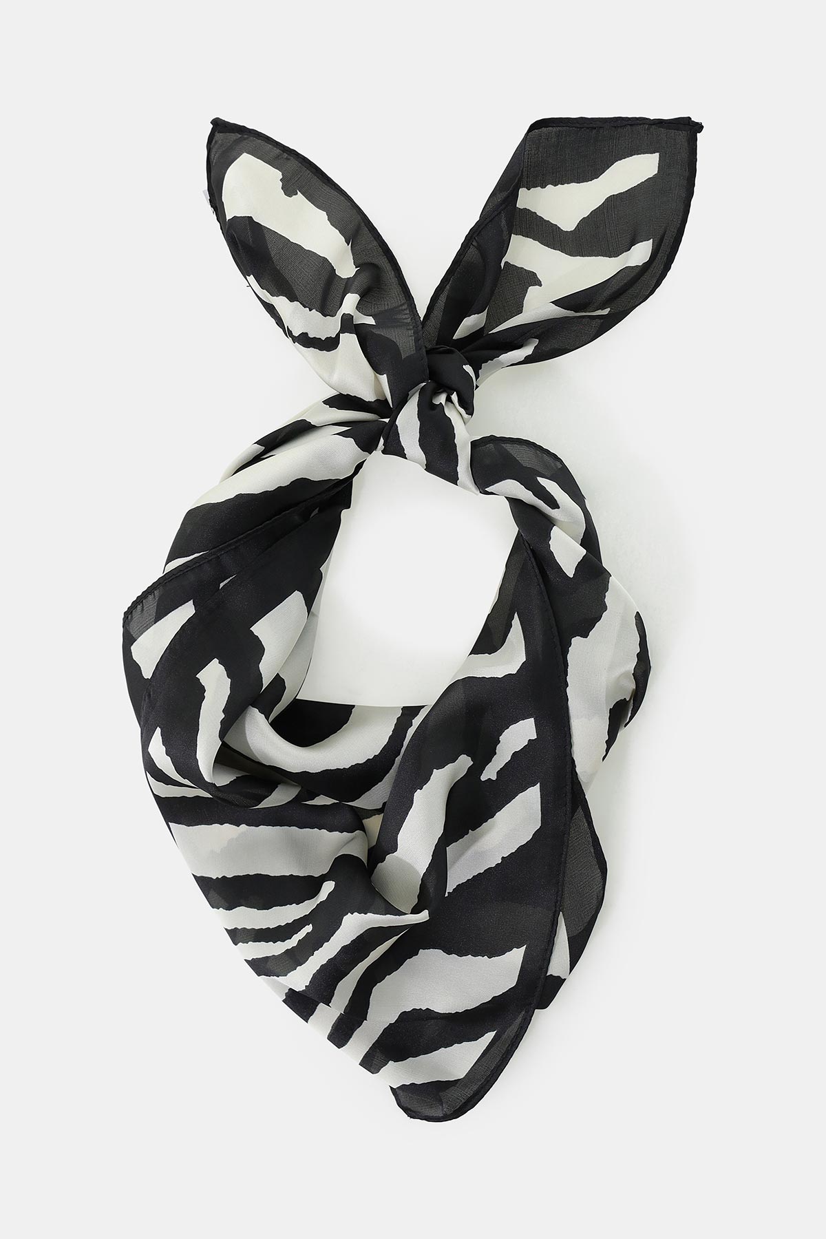 Black and white zebra-print silk square scarf tied in a knot, flat-lay on a white background