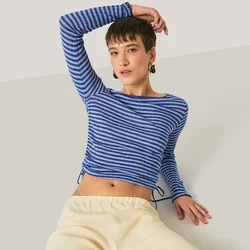 Giovane che si rilassa con un braccio dietro la testa, indossando una camicia a righe blu a maniche lunghe e pantaloni beige chiaro, su uno sfondo semplice.