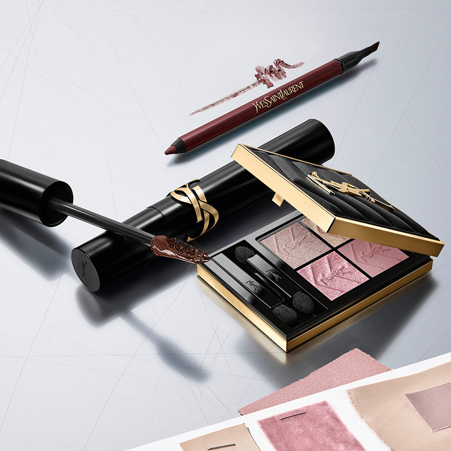 Composizione flat-lay con una palette YSL COUTURE CLUTCH (toni rosa/viola), una matita occhi nera e un mascara nero con logo Cassandre dorato.