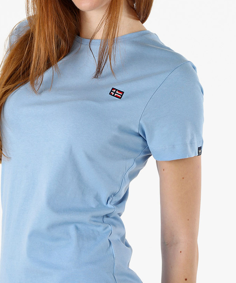 Woman wearing light blue crew-neck T-shirt with small rectangular flag patch on chest and long red hair visible