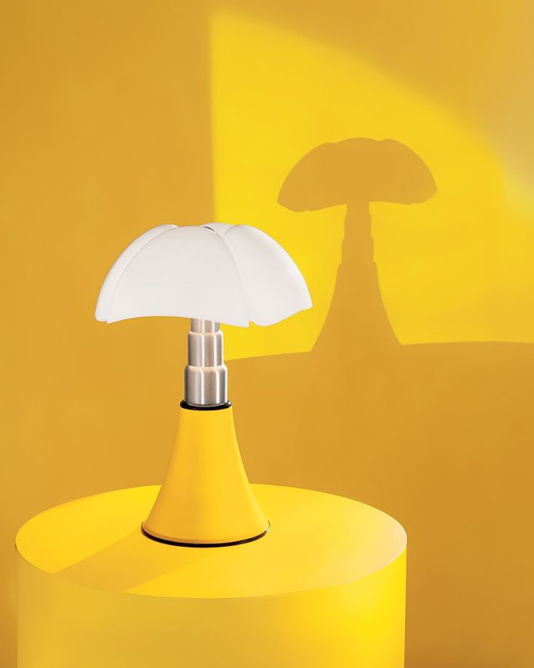 Yellow modern table lamp with white mushroom-shaped shade casting a distinct shadow on a bright yellow backdrop