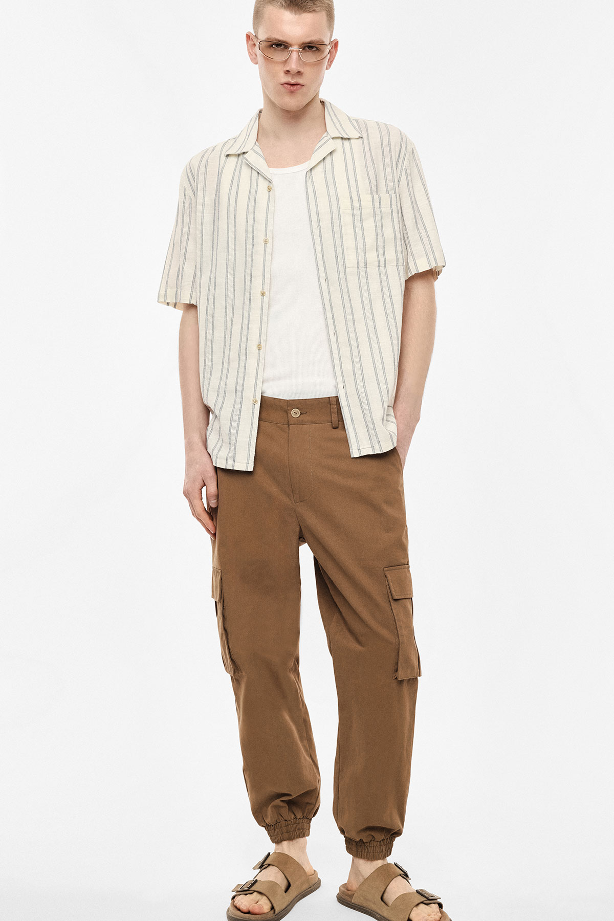 Young man modelling cream striped short-sleeve shirt over white tee, brown cargo trousers with elastic cuffs and sandals