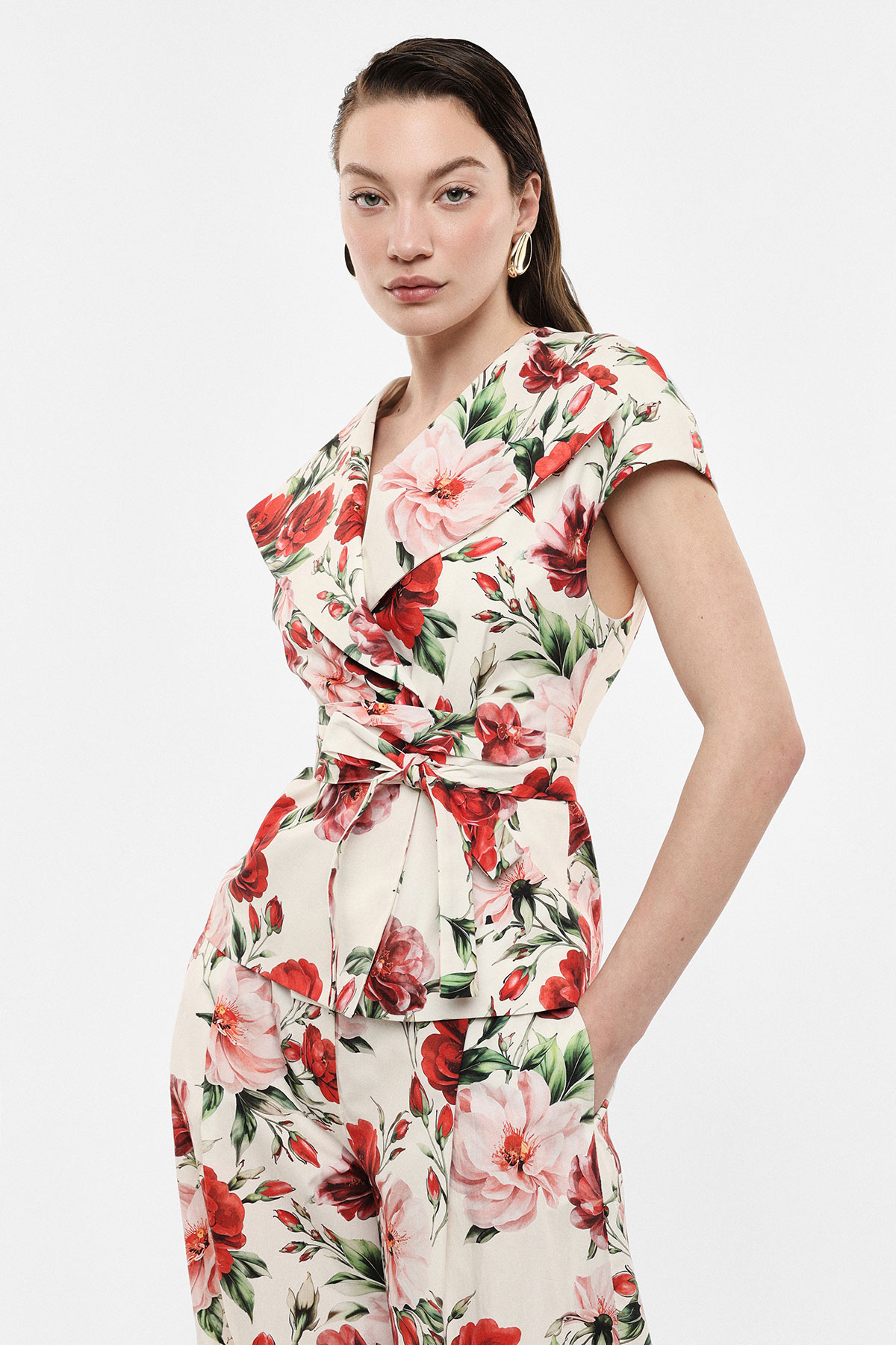Woman wearing cream floral wrap top and matching trousers with pink and red flowers, hands in pockets